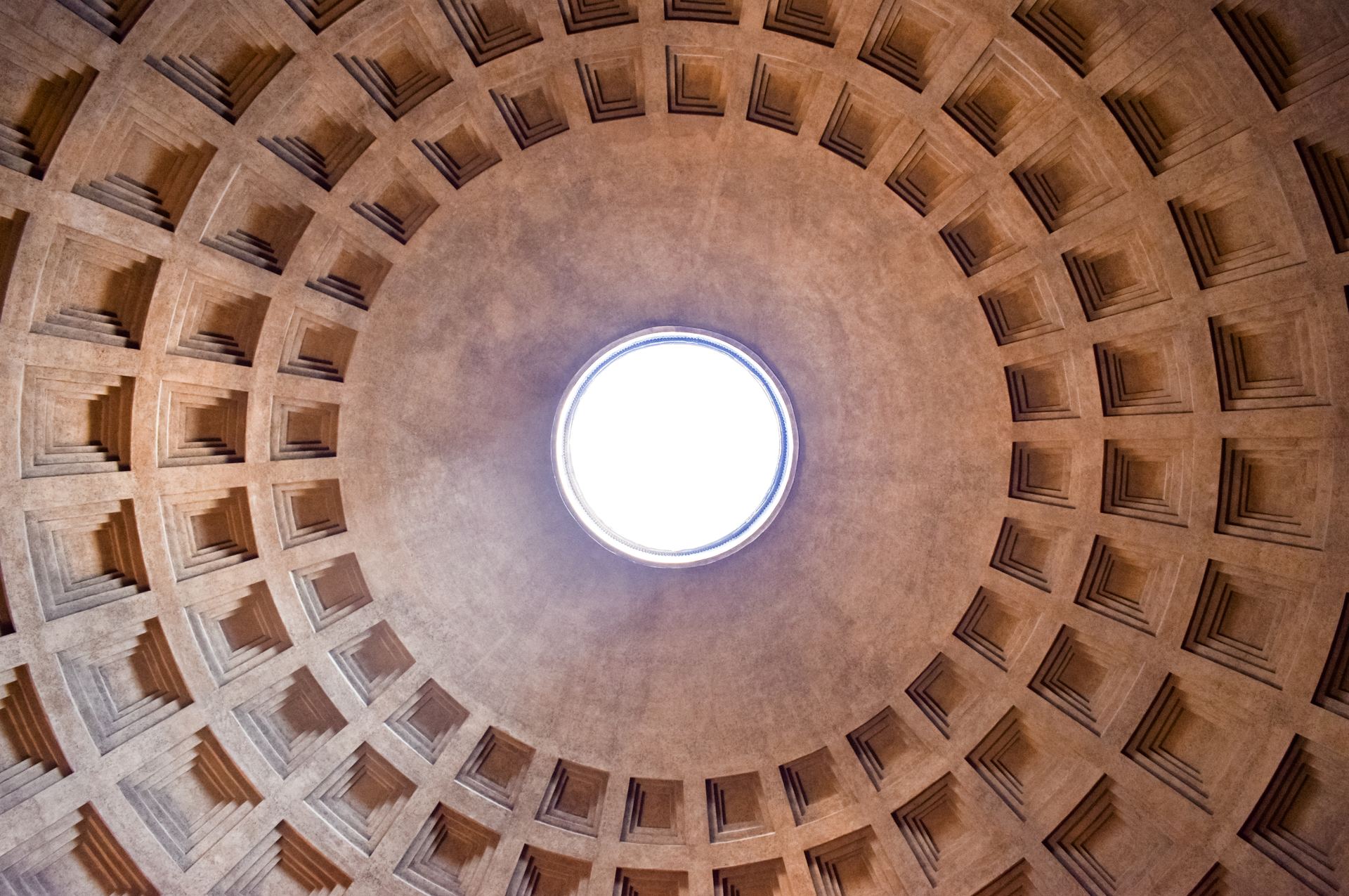 Looking straight up into the coffered concrete dome of the Pantheon in Rome, with rings of square sunken panels around the bright circular oculus