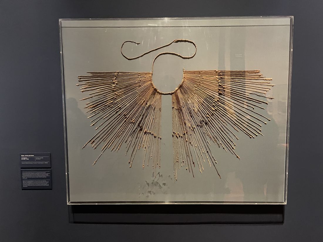 A khipu displayed in a glass case, with dozens of knotted cotton cords hanging from a single main cord in a fan shape