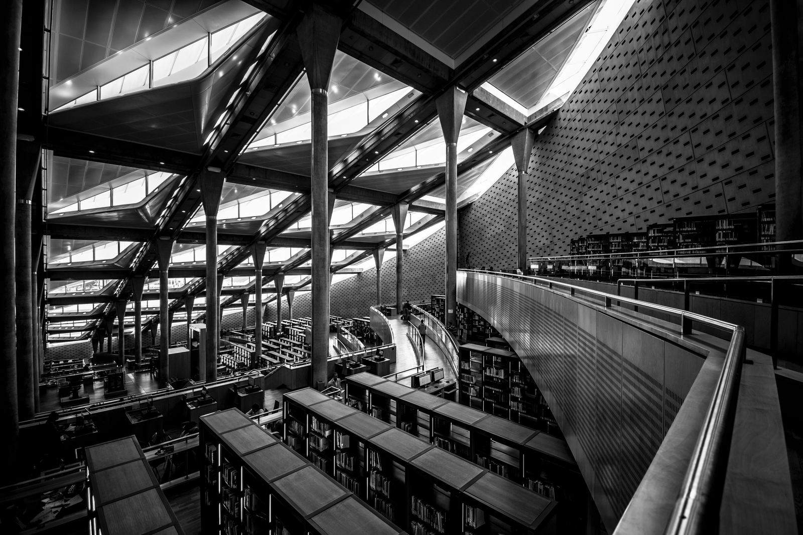 Black and white view of the vast terraced reading room of the Bibliotheca Alexandrina, with rows of desks under a slanted roof of skylights held up by tall slender columns