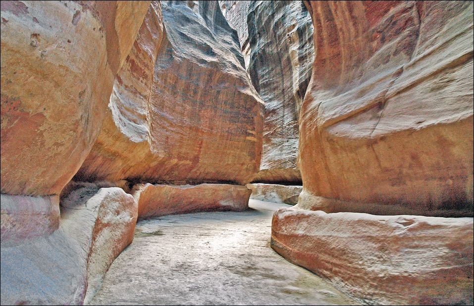 Rock-cut water channels running along both sides of the Siq canyon at Petra beneath tall sandstone walls