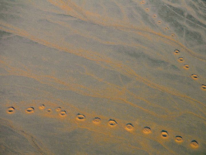 Aerial view of a desert plain near Isfahan, Iran, crossed by long curving lines of round qanat access shafts