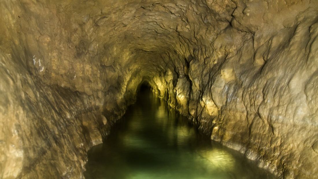 Inside a rough-walled underground qanat tunnel at Gonabad, with clear water flowing along its floor