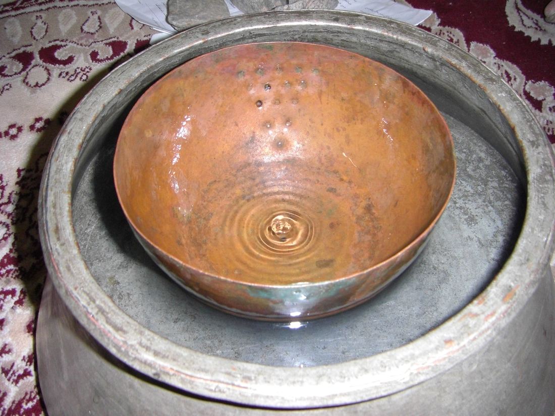 A copper bowl with a small hole floating in a larger metal basin of water, a traditional water clock used to time qanat water shares