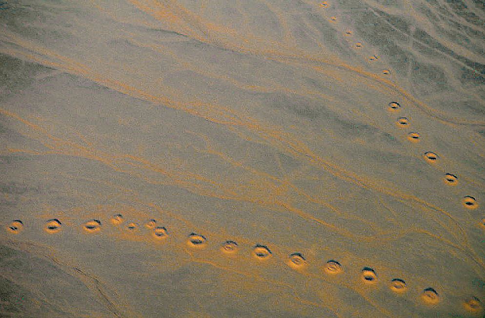 Aerial view of a desert plain near Isfahan, Iran, crossed by long curving lines of round qanat access shafts