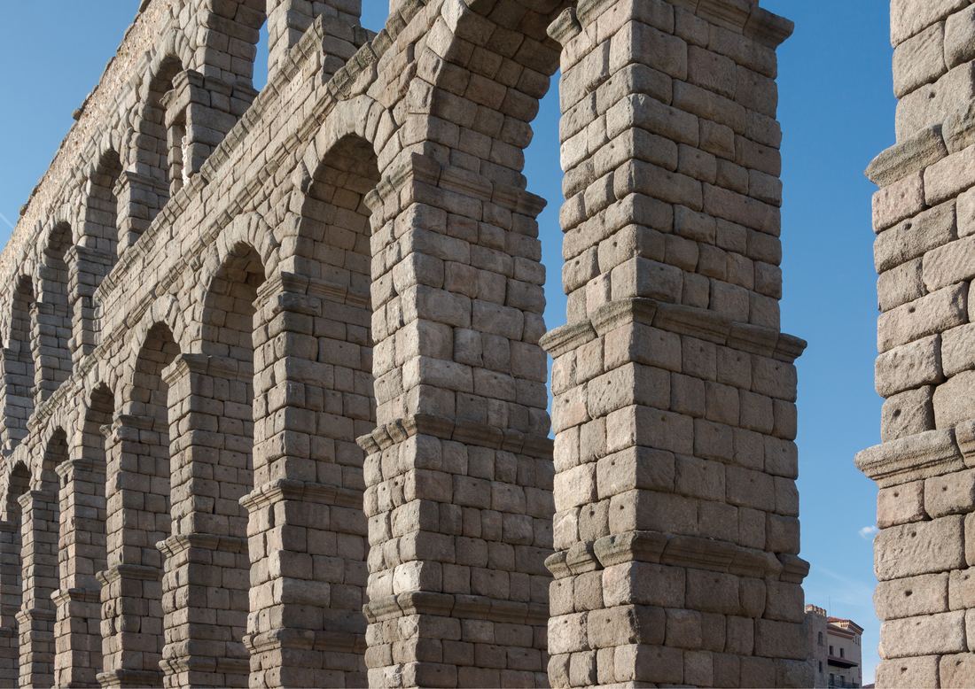 Close view of the tall granite arches of the Roman aqueduct of Segovia against a deep blue sky