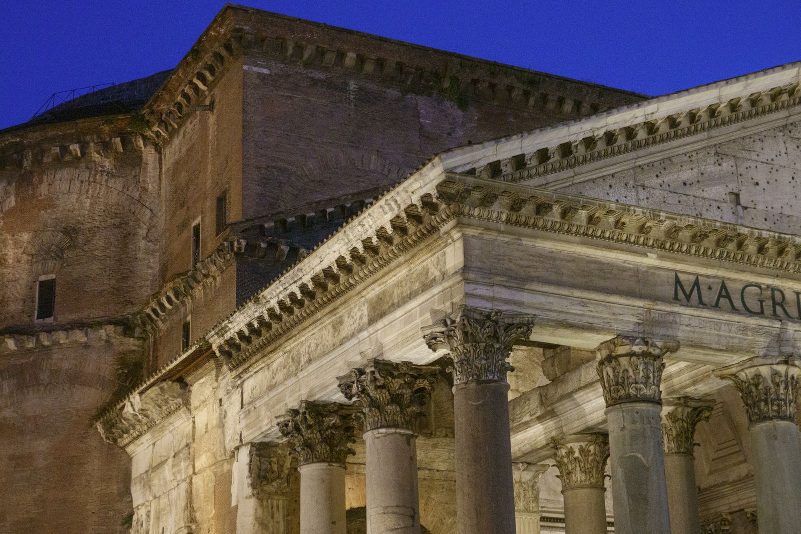 The columned portico and massive concrete drum and dome of the Pantheon in Rome against a deep blue evening sky