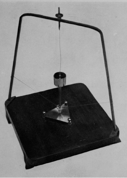 Black and white photo of a model of the seismoscope's inner workings, with a slender upright pendulum standing on a square base inside a frame